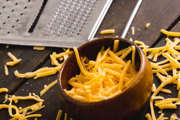 Poster Close-up of grated yellow cheese and bowl by grater on table, copy space © wavebreak3