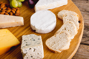 Close-up of various cheese with grapes and almonds on wooden board, copy space