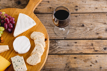 Overhead view of various cheese with grapes and red wine on wooden table, copy space
