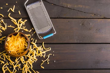 Tuinposter Directly above shot of grated yellow cheese and bowl by grater on wooden table, copy space © WavebreakMediaMicro