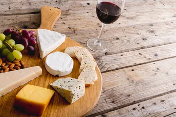 Tuinposter High angle view of various cheese with grapes and red wine on wooden table, copy space © wavebreak3