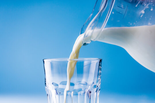 Close-up of milk being poured in glass from jar against blue background, copy space