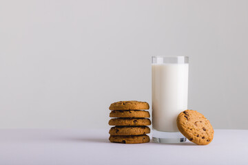 Milk in glass by cookies against white background, copy space