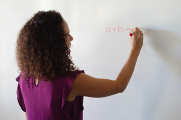 Caucasian young female teacher writing formula on whiteboard during math class in school
