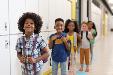 Portrait of multiracial smiling elementary school children with backpacks standing in row
