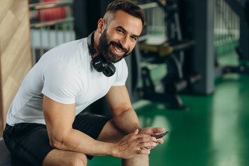 Young handsome man using phone while having exercise break in gym