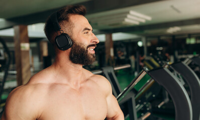 Athletic muscular man in wireless headphones listening music during training in gym