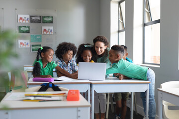 Caucasian young female teacher teaching laptop to african american elementary students