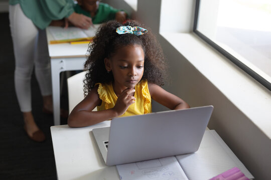 African american elementary schoolgirl using laptop at desk in classroom during computer class