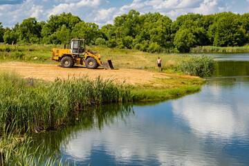 tractor rakes sand on the river beach in summer