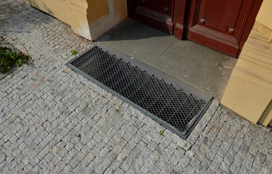 metal grating at the entrance to the building. is embedded below the surface. paving marble cubes. cobblestone brown historic building door