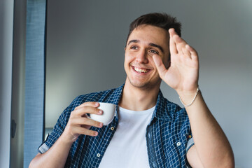 A young man using his phone to talk and write messages and drinking coffee while standing next to a...
