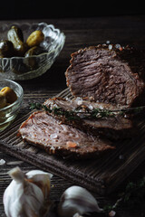 Baked roast beef with pickled cucumbers and olives on a wooden table