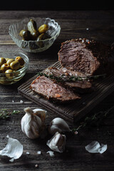 Baked roast beef with pickled cucumbers and olives on a wooden table