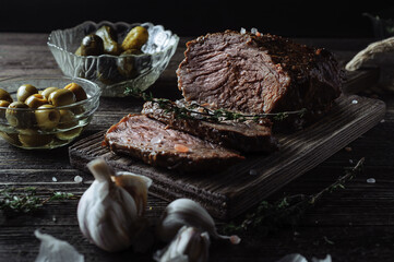 Baked roast beef with pickled cucumbers and olives on a wooden table