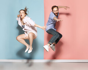 Young couple, emotional man and pretty woman messing about isolated over blue and pink background. Human emotions, youth, love and active lifestyle concept