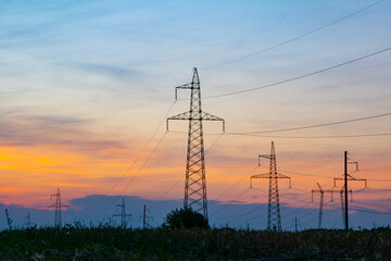 A high-voltage tower in the middle of a wheat field, against the background of a warm summer sunset
