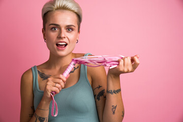 Sexy dominant caucasian woman feeling surprised with pink biting whip over rose background
