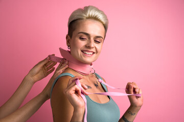 Unrecognizable hands fastening bdsm collar at cheerful woman isolated on pink studio background