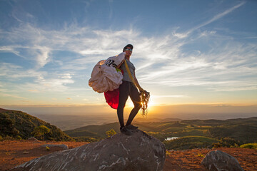 Woman holding paraglider on top of the mountain at sunset, Brazil