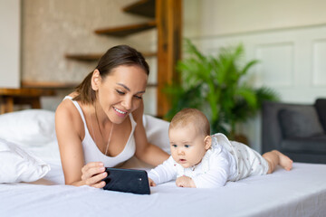 Young mother with newborn daughter watching cartoons through smartphone online application.