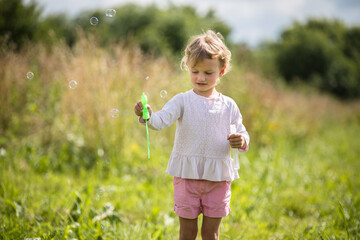 Beautiful little girl, has happy fun cheerful smiling face, soap bubble blower.