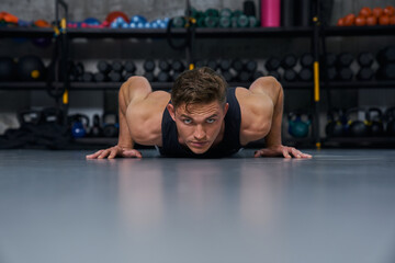 Fototapeta na wymiar Muscular man doing push up exercises during intense fitness workout in grungy gym