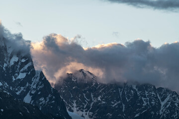 Beautiful mountains landscape on the sunset. High snow covered mountains in the fog and clouds.