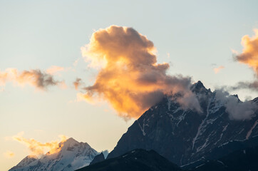 Fototapeta premium Beautiful mountains landscape on the sunset. High snow covered mountains in the fog and clouds. 