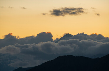 Beautiful mountains landscape on the sunset. High snow covered mountains in the fog and clouds.