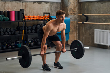 Fototapeta na wymiar Muscular shirtless guy bodybuilder exercising with heavy barbell at gym
