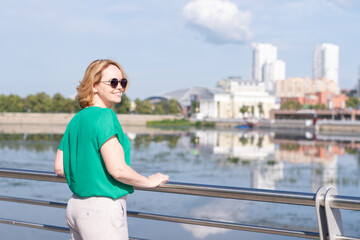 A view from the back of a girl in a green blouse standing on the riverbank against the background of a blurred city. A girl walks through the streets of the city.