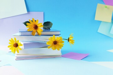 A stack of books with bookmarks from fresh chamomile flowers, on the background of note paper in pastel colors, the concept of education, back to school, reading, library, congratulation, postcard