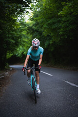 Professional female cyclist trains in the woods. Woman riding race bicycle on a forest asphalt...