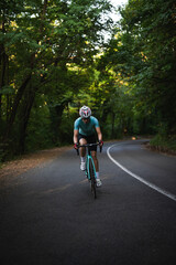 Professional female cyclist trains in the woods. Woman riding race bicycle on a forest asphalt road, uphill, front view
