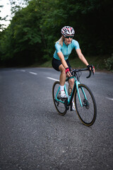 Fototapeta premium Professional female cyclist trains in the woods. Woman riding race bicycle on a forest asphalt road, uphill, front view