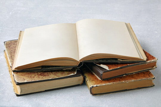 An Open Vintage Book With Blank Pages Or A Dust Jacket Notebook On A Stack Of Old Shabby Books On A Gray Concrete Table