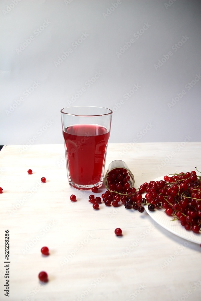 Wall mural fallen berries of red currant on wooden white table and galss of juice