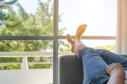 Women legs on the sofa couch. Woman feet up against window. Young woman lying on bed against window.Young woman lying on the bed with raised legs up, against the windows. Copy space