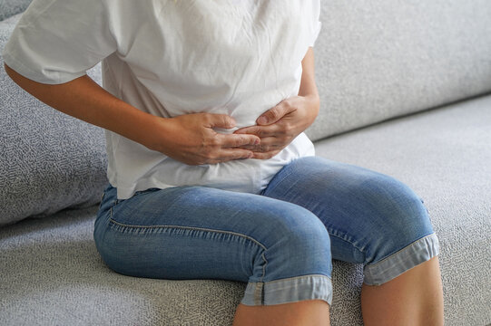 Woman siting on sofa and holding her hands on her stomach. Woman having painful stomachachem, menstruation. Pain in the abdomen of a woman. Body and health care concept
