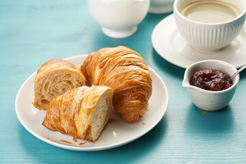 Two french soft croissants on a white plate on a blue wooden table, a cup of black coffee in white...