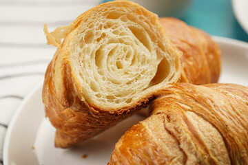 Two french soft croissants on a white plate on a blue wooden table, a cup of black coffee in white sophisticated cup, milk, sugar, jam, close-up