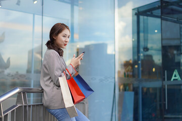 Smiling Asian woman with colored shopping bags on shopping mall background and looking happy Smiling shopping while standing in front of a department store lifestyle concept