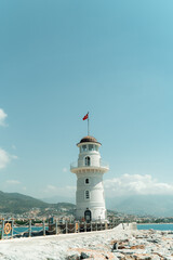 Fototapeta na wymiar Lighthouse in the port of Alanya. white lighthouse in seaport of Alanya with concrete path and stones