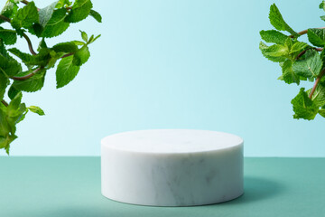 White marble cosmetic podium on light blue background with aromatic mint leaves. © Iryna