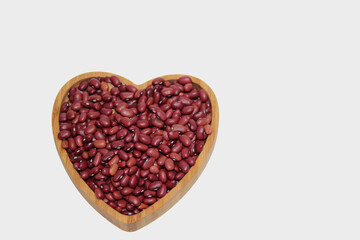 Kidney beans in a wooden heart-shaped bowl on white background, top view and with copy space.