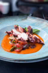 Fried octopus in tomato sauce with olives and capers in a blue plate. Delicious traditional Italian dish. Dinner at a fish restaurant.