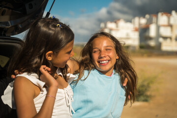 Smiling little sisters embracing and chatting while spending time together near the car