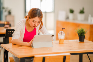 Happy Asian female student wearing headphones, studying online, watching webinars, podcasts on tablets, listening, learning, education courses. online meeting