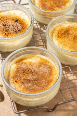 Sweet creme brulee dessert. Portioned glass jars with homemade creme brulee with caramel topping, on beige colored background with sugar in spoon and vanilla copy space